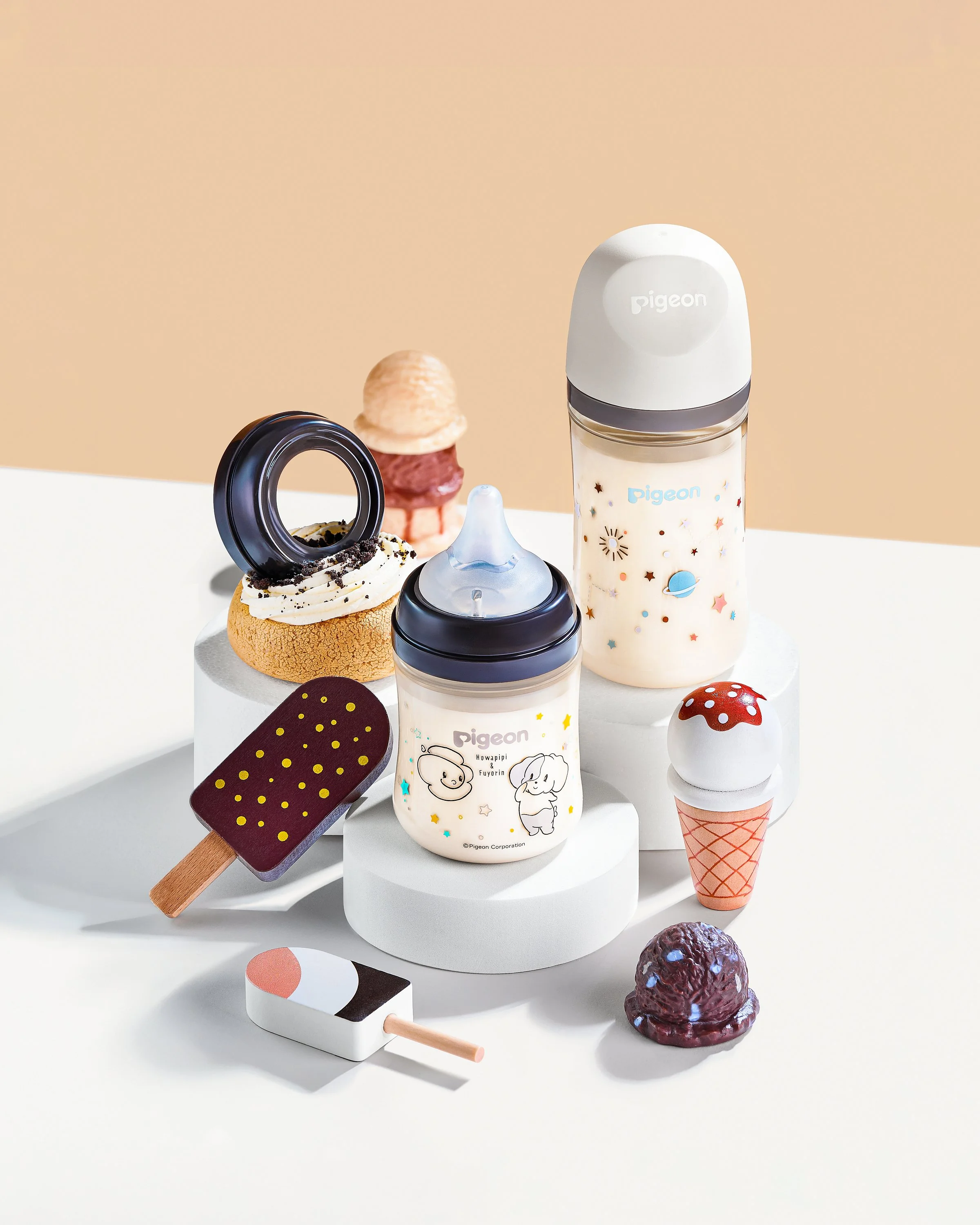 Collection of baby bottles, a popsicle toy, and plush ice cream toy on a white surface with a beige wall background.