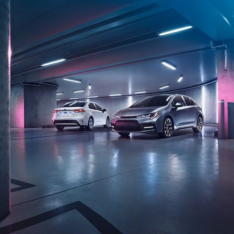 Two sedans parked in an underground parking garage with modern lighting and concrete pillars, illuminated by blue and pink lights.