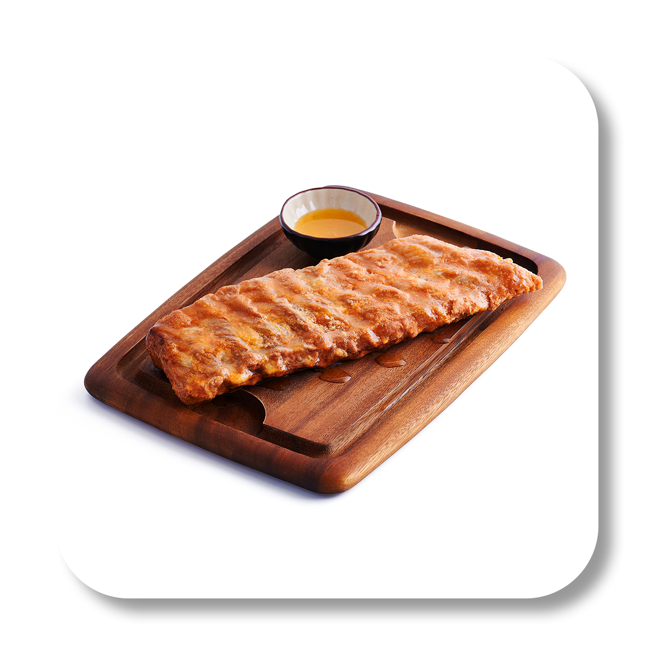 A grilled rack of ribs on a wooden serving board with a small bowl of dipping sauce.