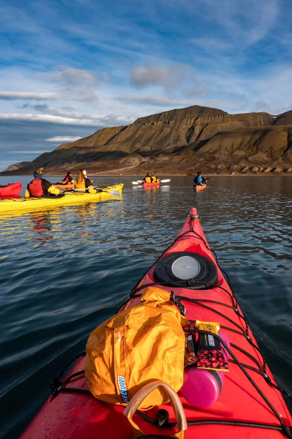 A red kayak drifts in the water whilst Adventfjorden mountain looms up ahead