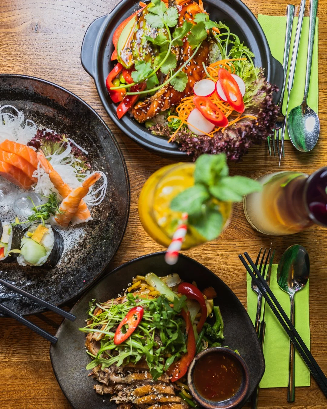 Bunte asiatische Gerichte mit Sushi, Fleisch, Salat und Getränken auf einem Holztisch