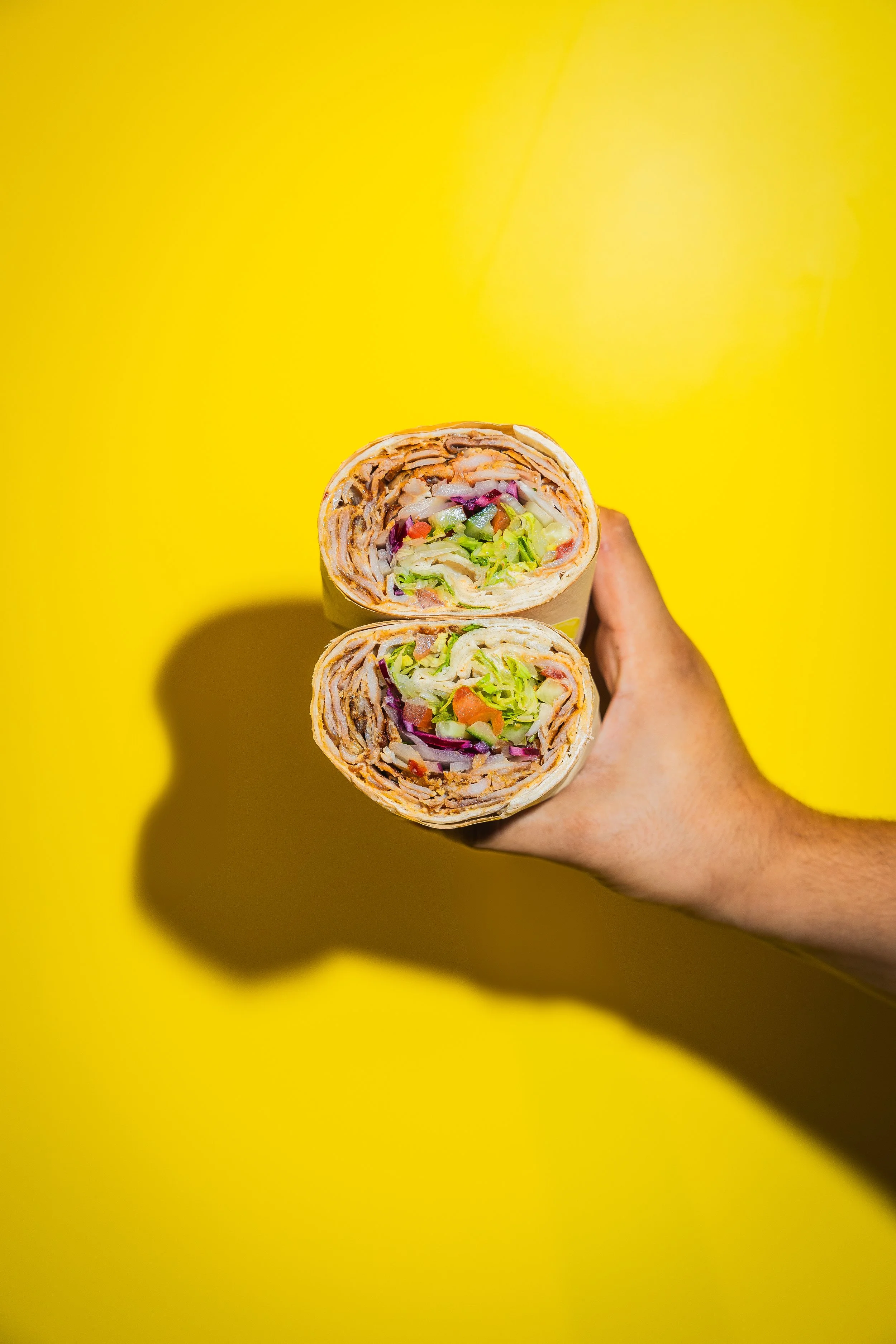 Hand hält zwei geschnittene Wraps mit Salat und Gemüse gegen einen gelben Hintergrund.