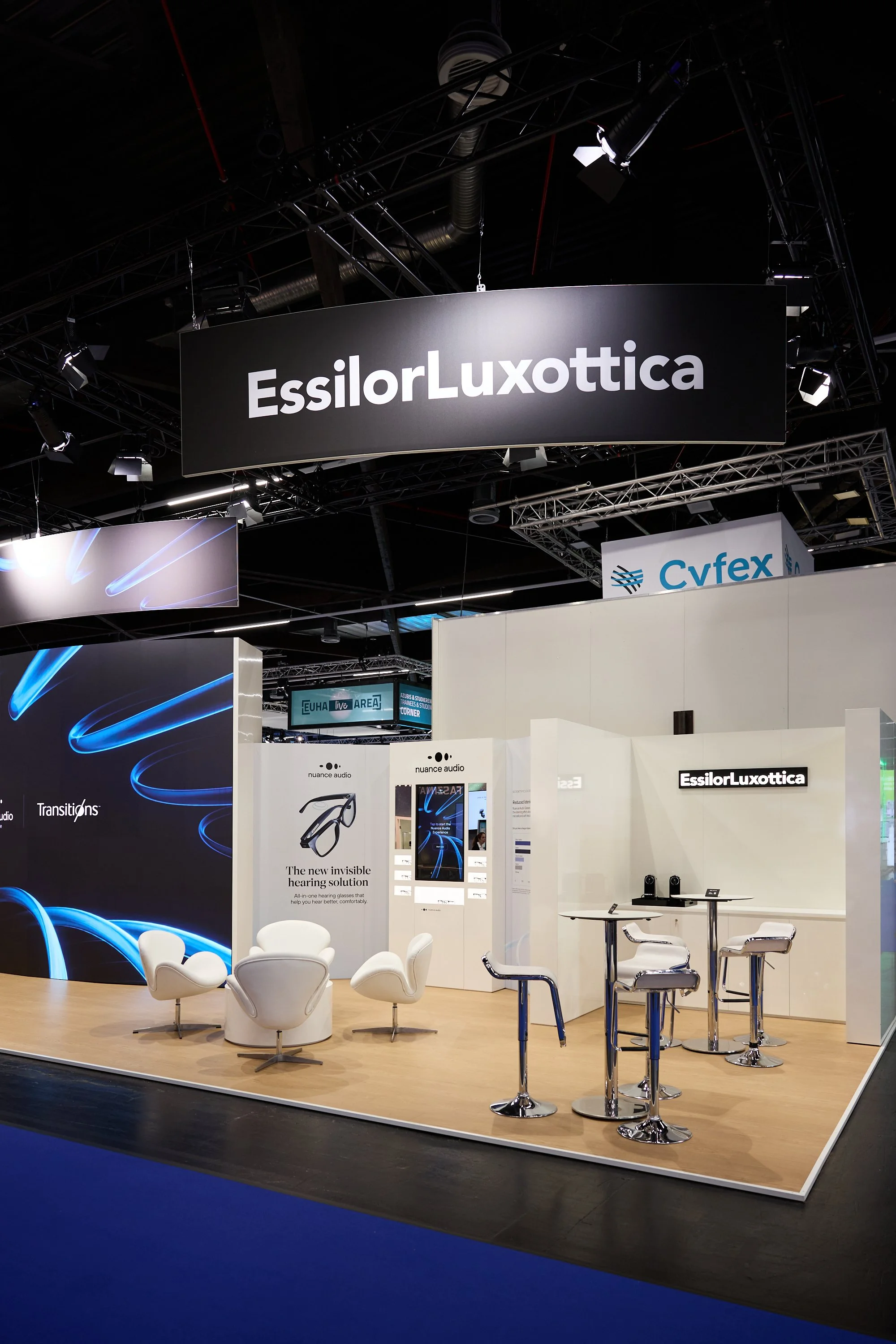 Messestand von EssilorLuxottica mit Sitzgelegenheiten, Informationsbildschirmen und Produkten, auf einer Messe gezeigt.