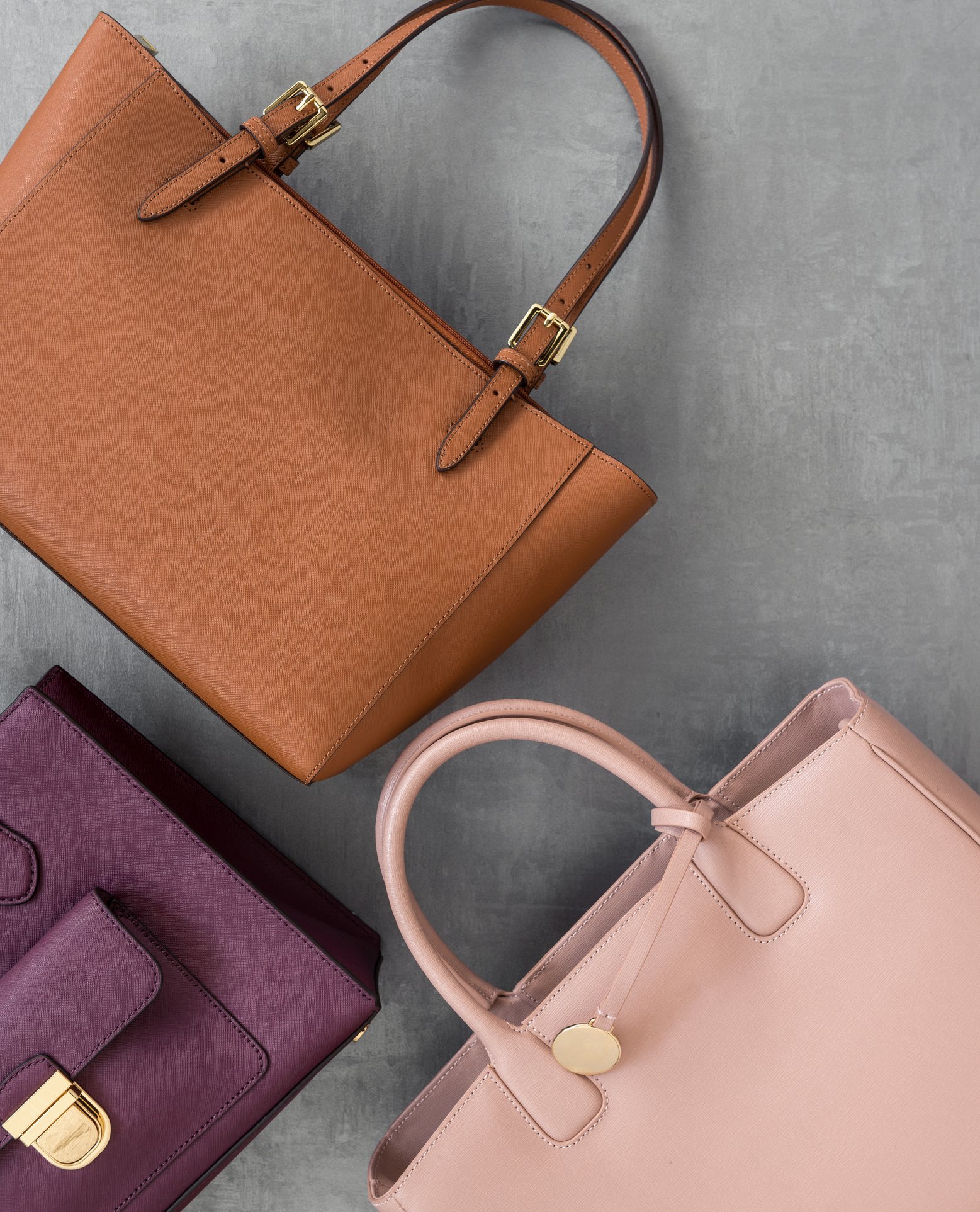 Three handbags in beige, purple, and blush pink placed on a gray surface.