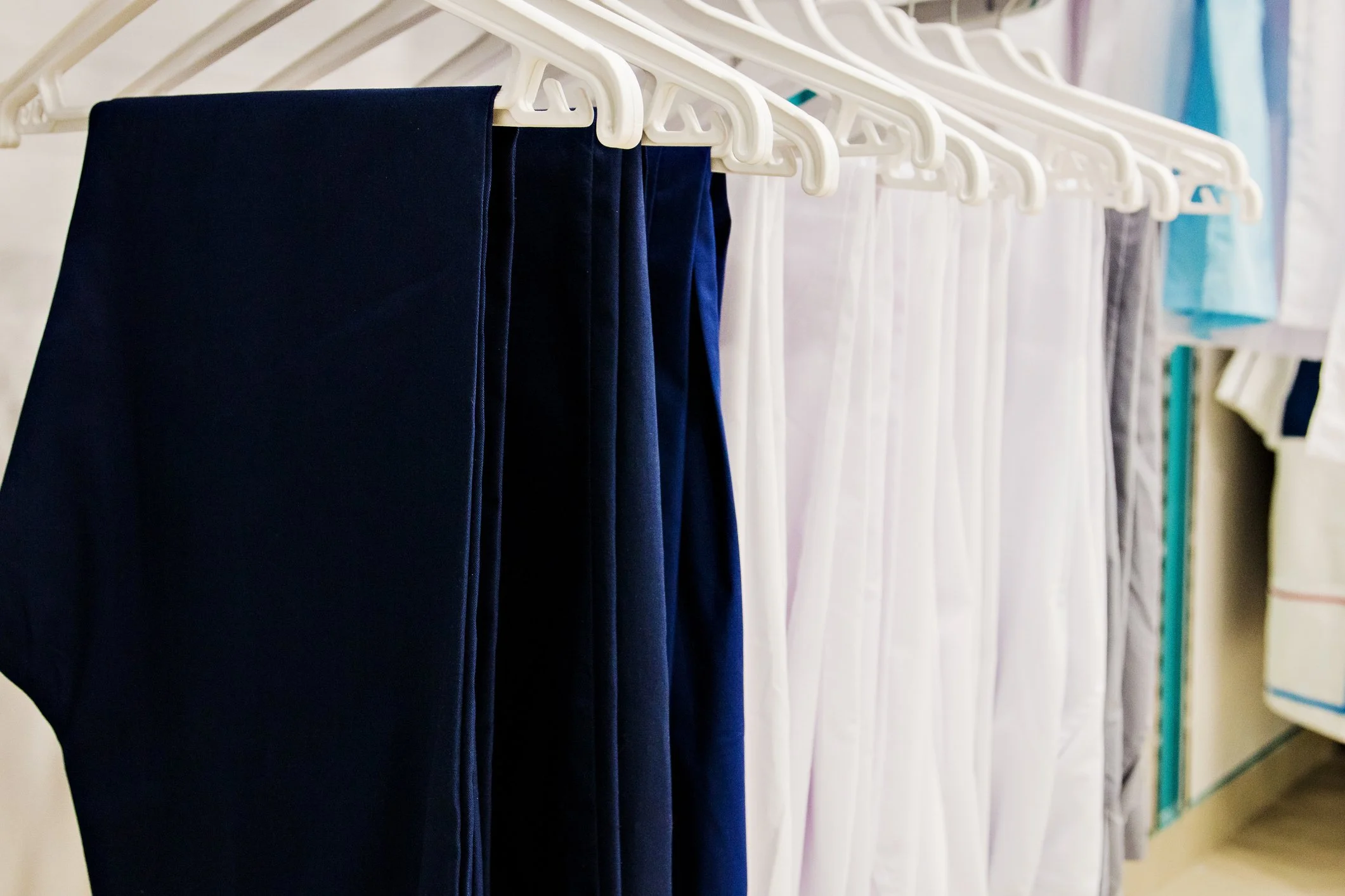 Tablecloths hanging on a rack, including dark blue and white fabrics, in a retail or laundry setting.