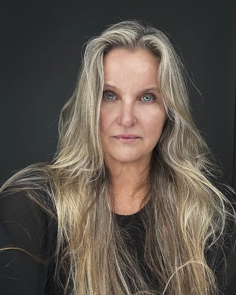 Close-up headshot of photographer Alex Abercrombie with long blonde hair against a dark gray background.