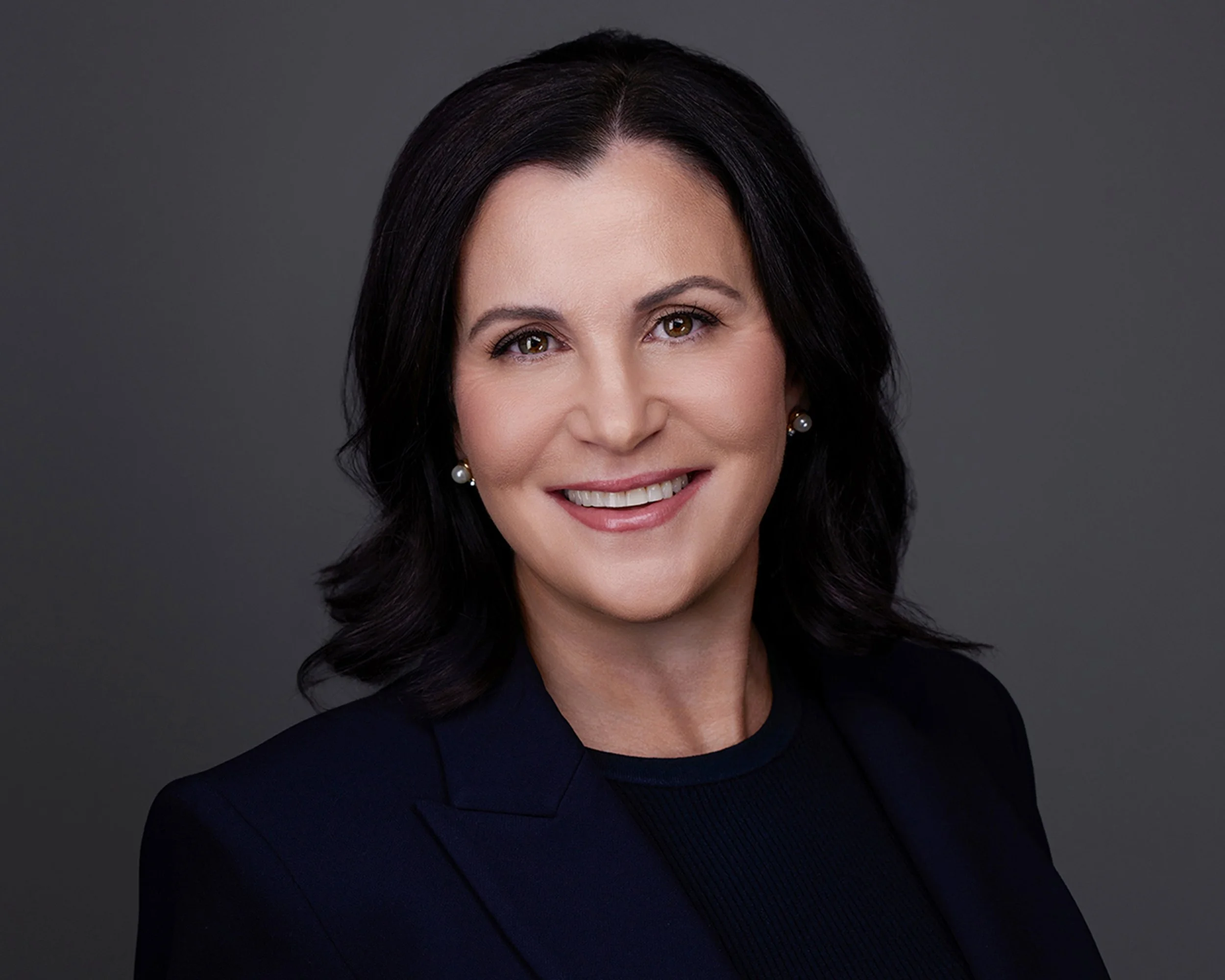 Professional executive headshot photographed in studio with soft lighting and a dark gray background, creating a polished and approachable look for corporate branding and LinkedIn profiles.