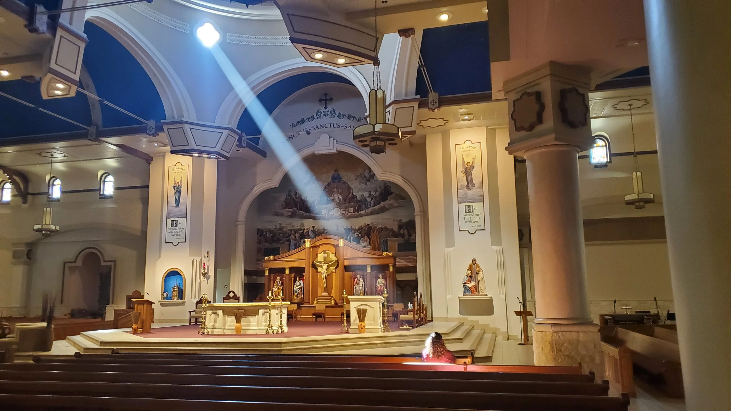 Close-up of a person's hand holding a pen and writing in a notebook on a desk, with a computer mouse, a cup, and a keyboard in the background.