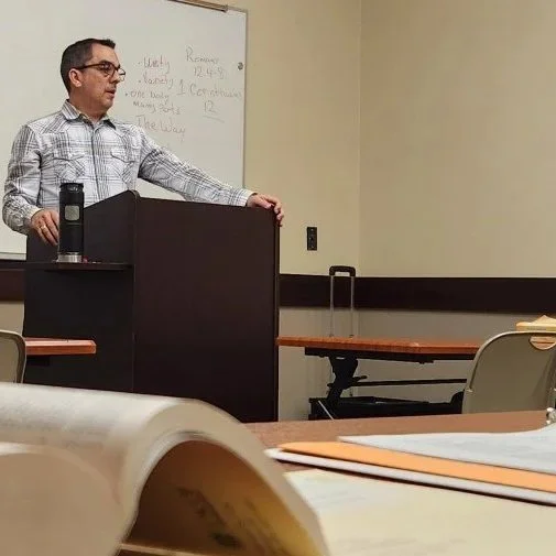 A man is teaching behind a small podium in a classroom.