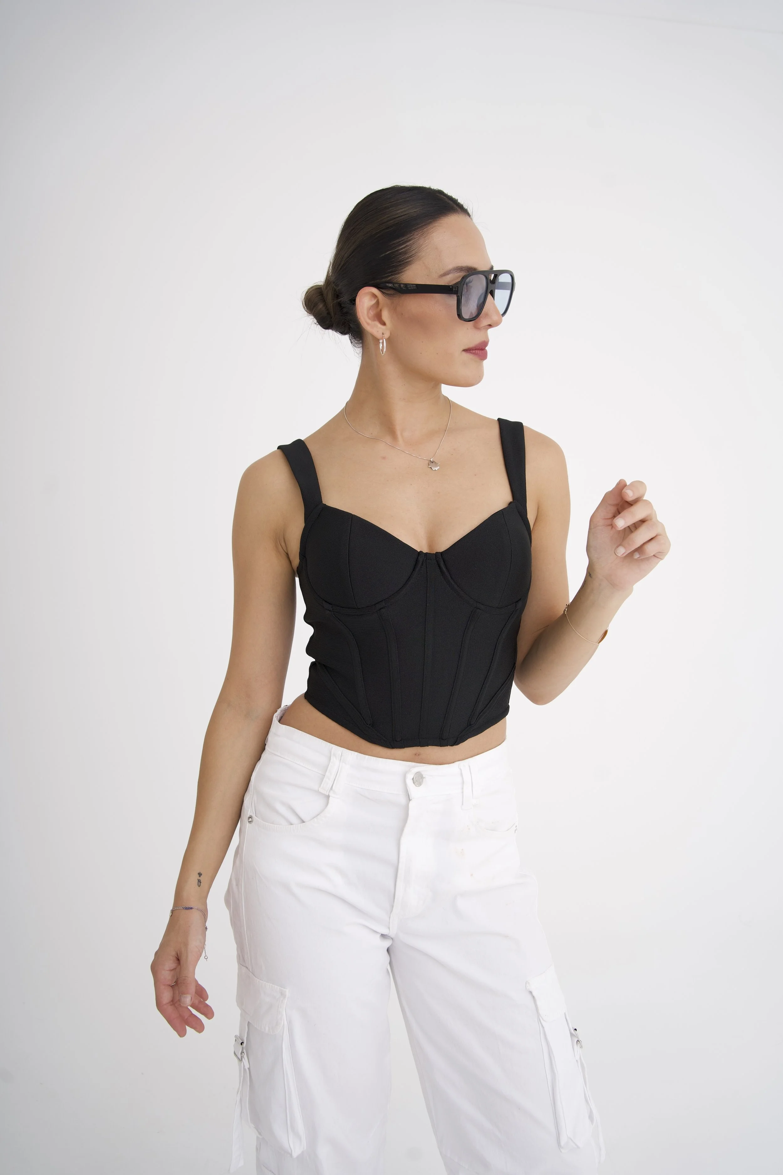 Ning-Ning with her dark hair in a bun, wearing sunglasses, a black sleeveless top, and white cargo pants, against a plain white background, for a DJ portrait shot.
