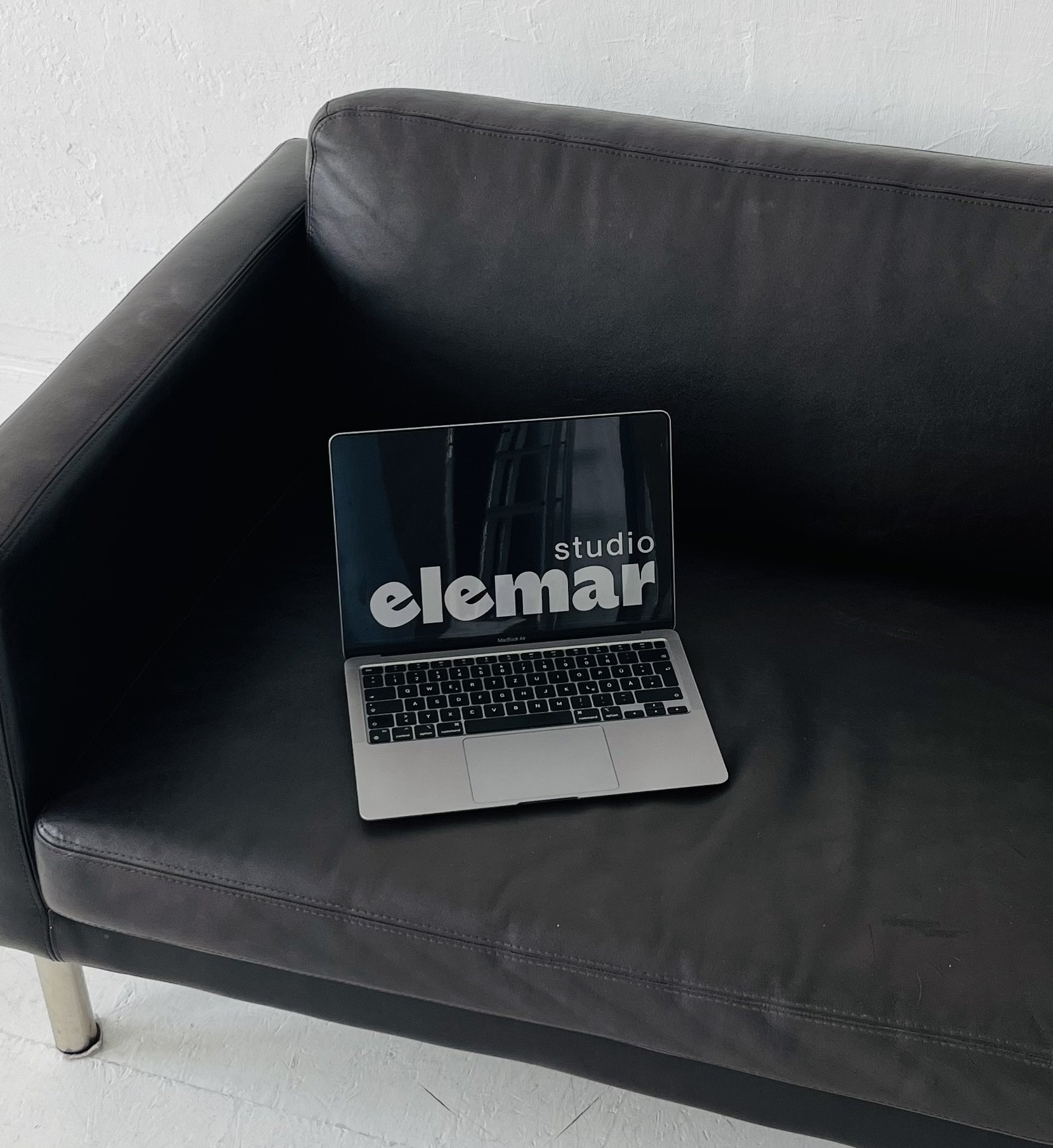 Laptop displaying elemarstudio logo on a black couch