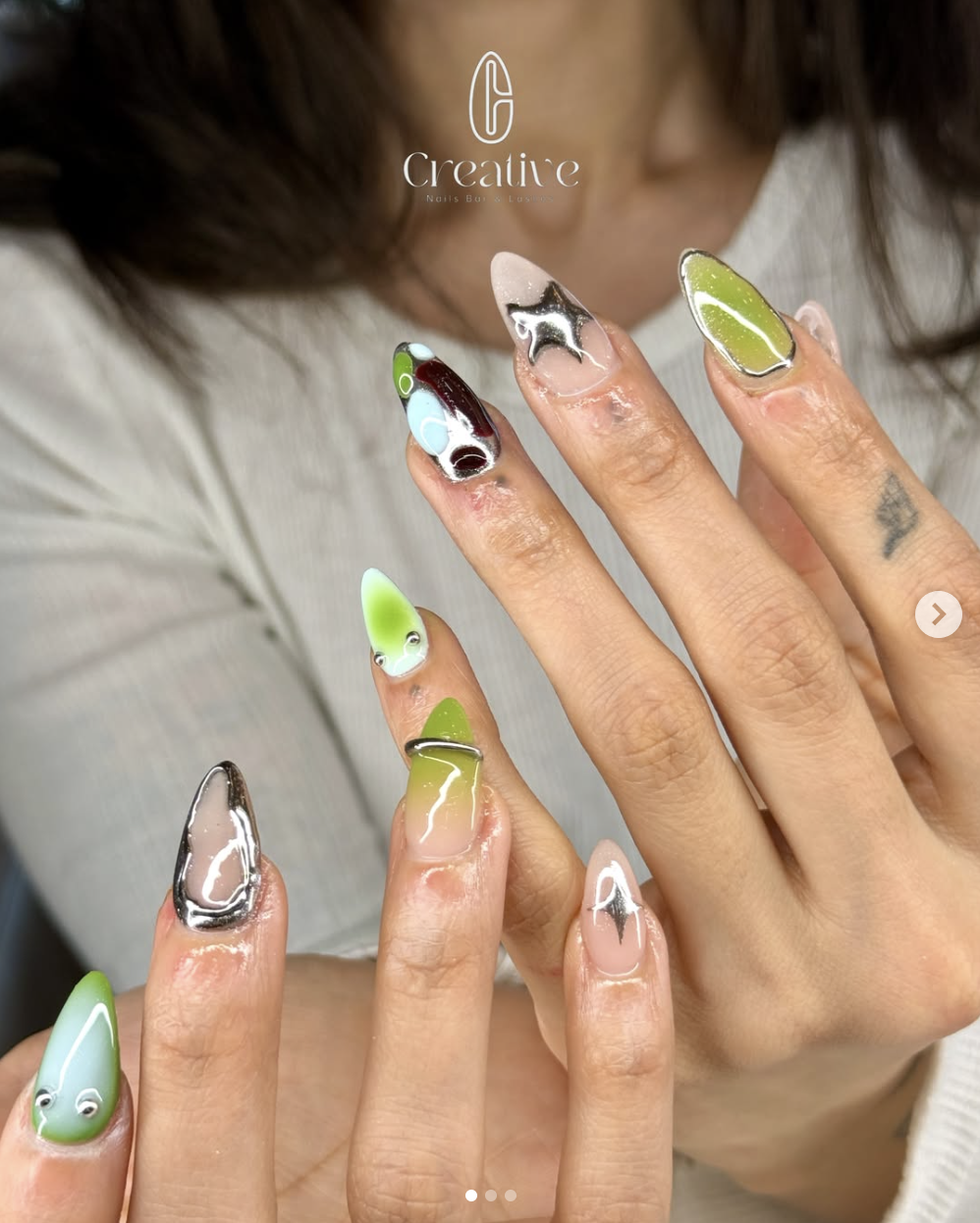 Close-up of a woman's hand with colorful, artistic nail art on her fingernails, featuring various abstract designs, patterns, and colors.
