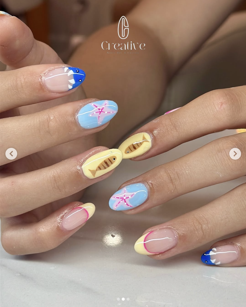 Nail art with various summer-themed designs including fish, starfish, and waves in bright colors.