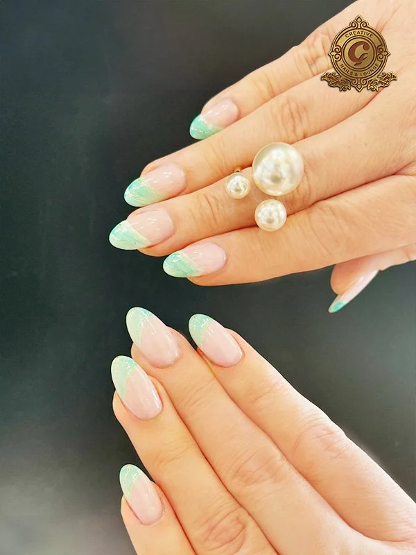 Hands with pastel nail art featuring a blue gradient design, wearing a ring with pearl accents on a dark background.