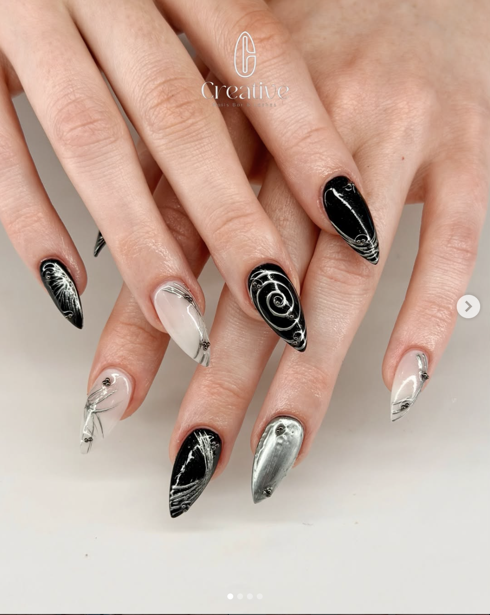 Nail art with black, white, and silver marbled designs on long, almond-shaped nails.