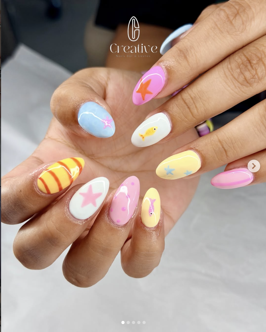 Colorful nail art with pastel and bright colors, featuring designs like fish, starfish, star, and striped patterns, arranged in a beach or ocean theme.