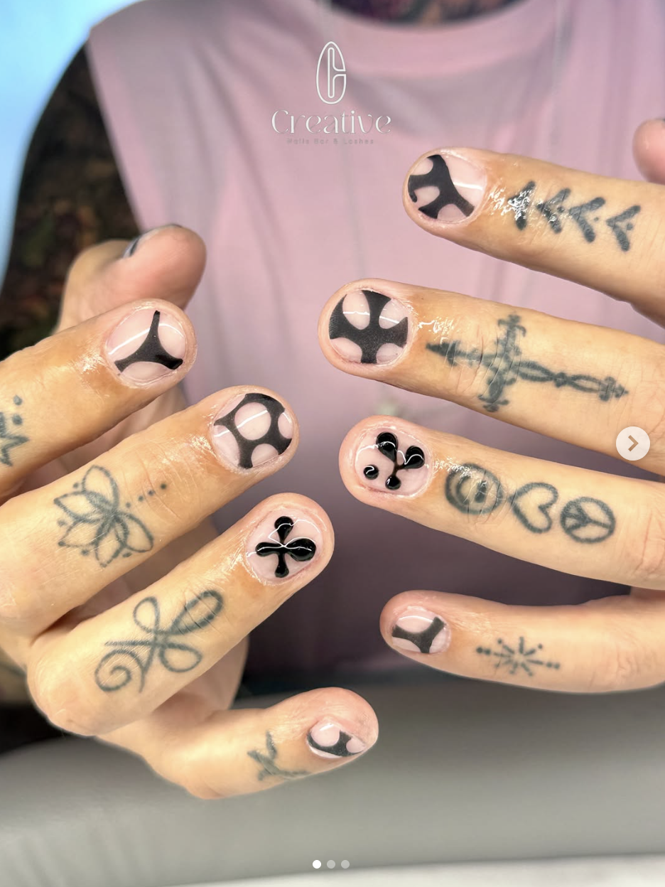Close-up of hands with tattoos and black and white nail art featuring symbols like peace signs, hearts, and abstract designs.