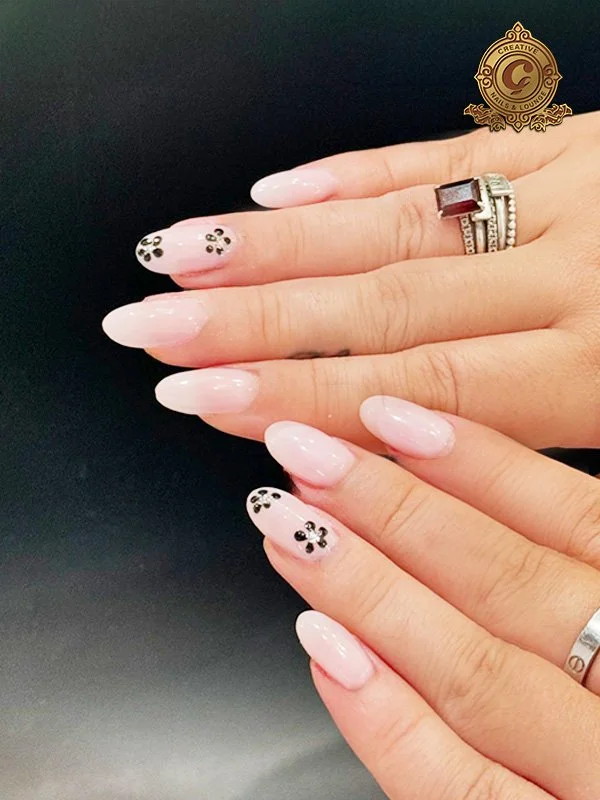 Hands with elegant pink manicure, floral nail art on one finger, wearing silver rings.