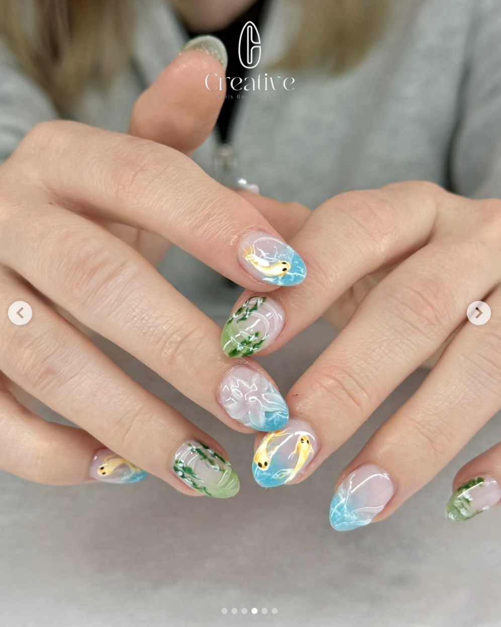 Close-up of hands with colorful nail art featuring ocean-themed designs, including fish, seaweed, and water effects.