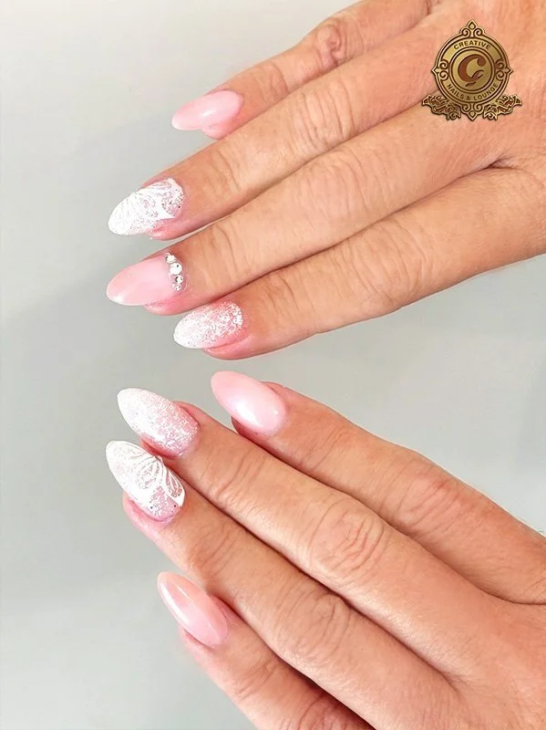 Elegant pink and white nail art with rhinestones and intricate designs.