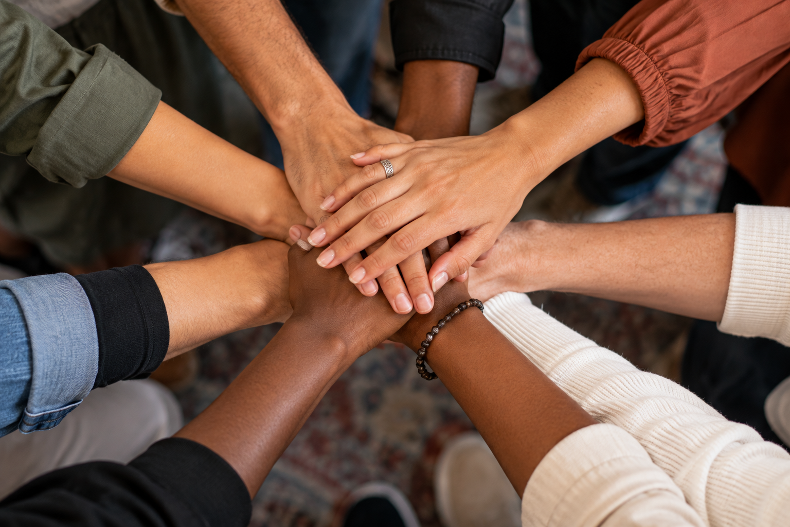 Multiple diverse hands stacked together in a show of unity and teamwork.