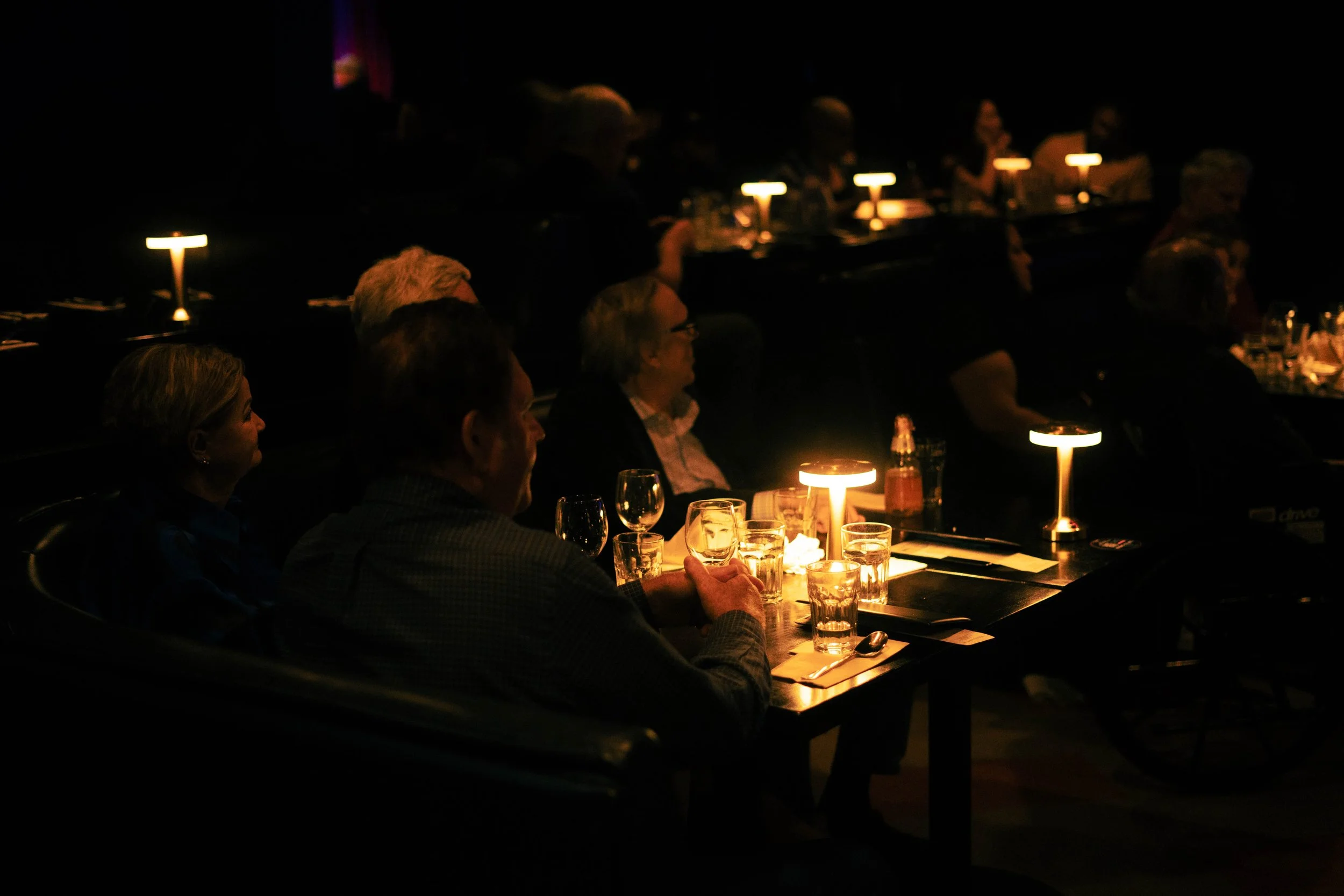 People sitting at a dimly lit restaurant table with glasses and candles.