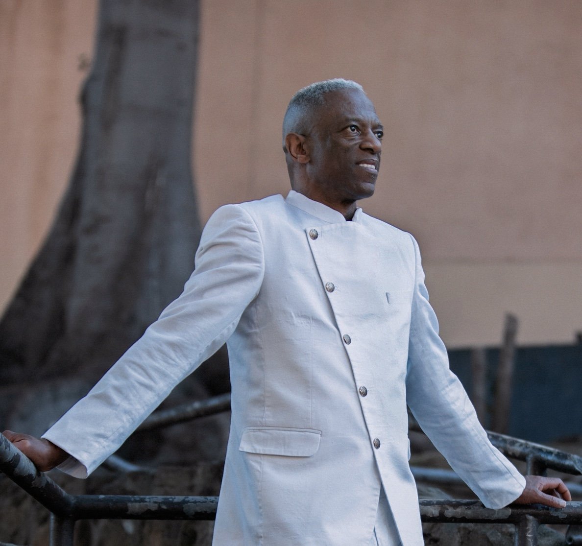 A man dressed in a white chef's coat standing outdoors with his arms resting on a metal railing, looking to the side. Earl Thomas.