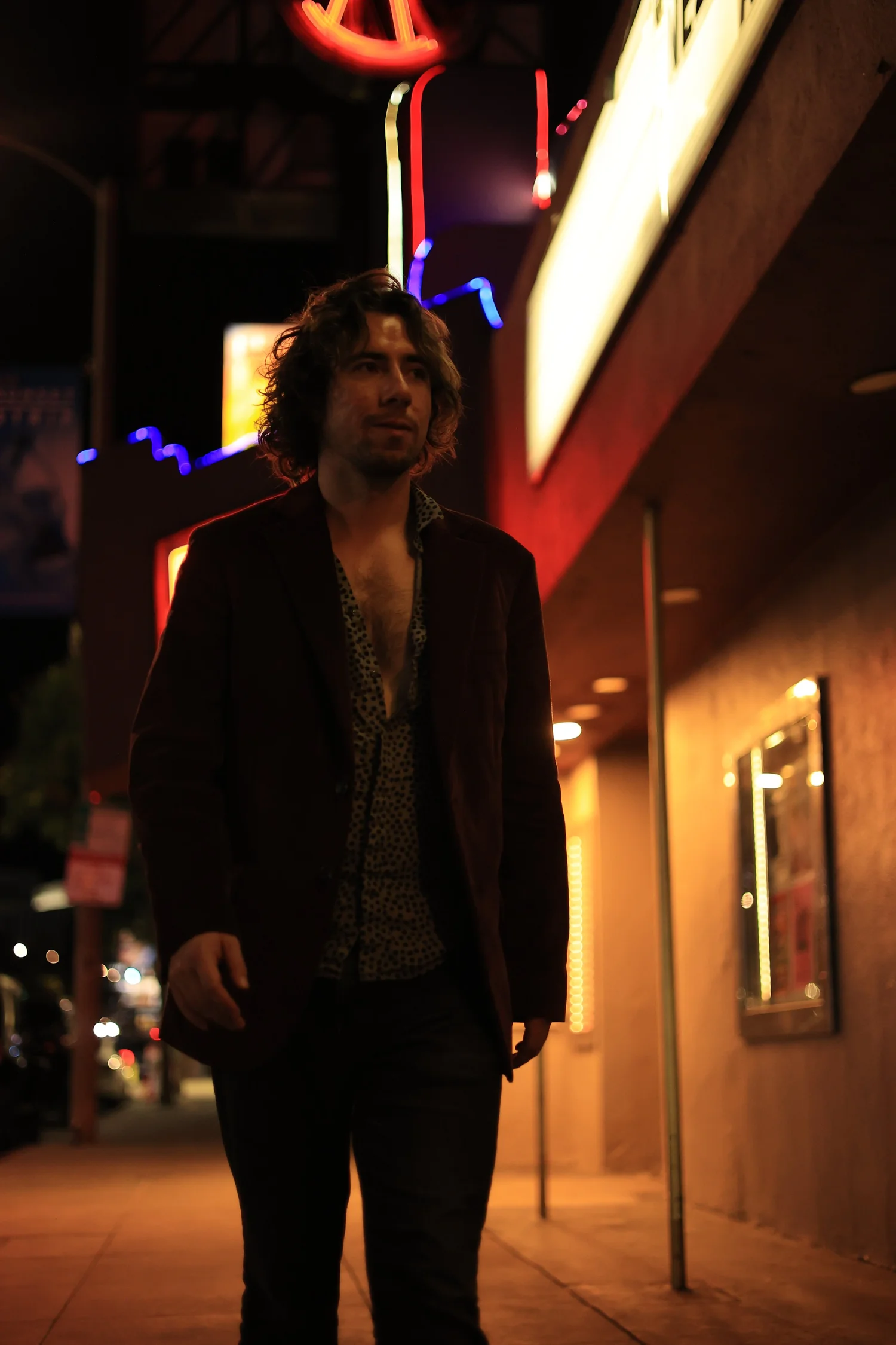 Harrison Flynn stands beside a lit swimming pool at night in a wide brim hat and dark jacket