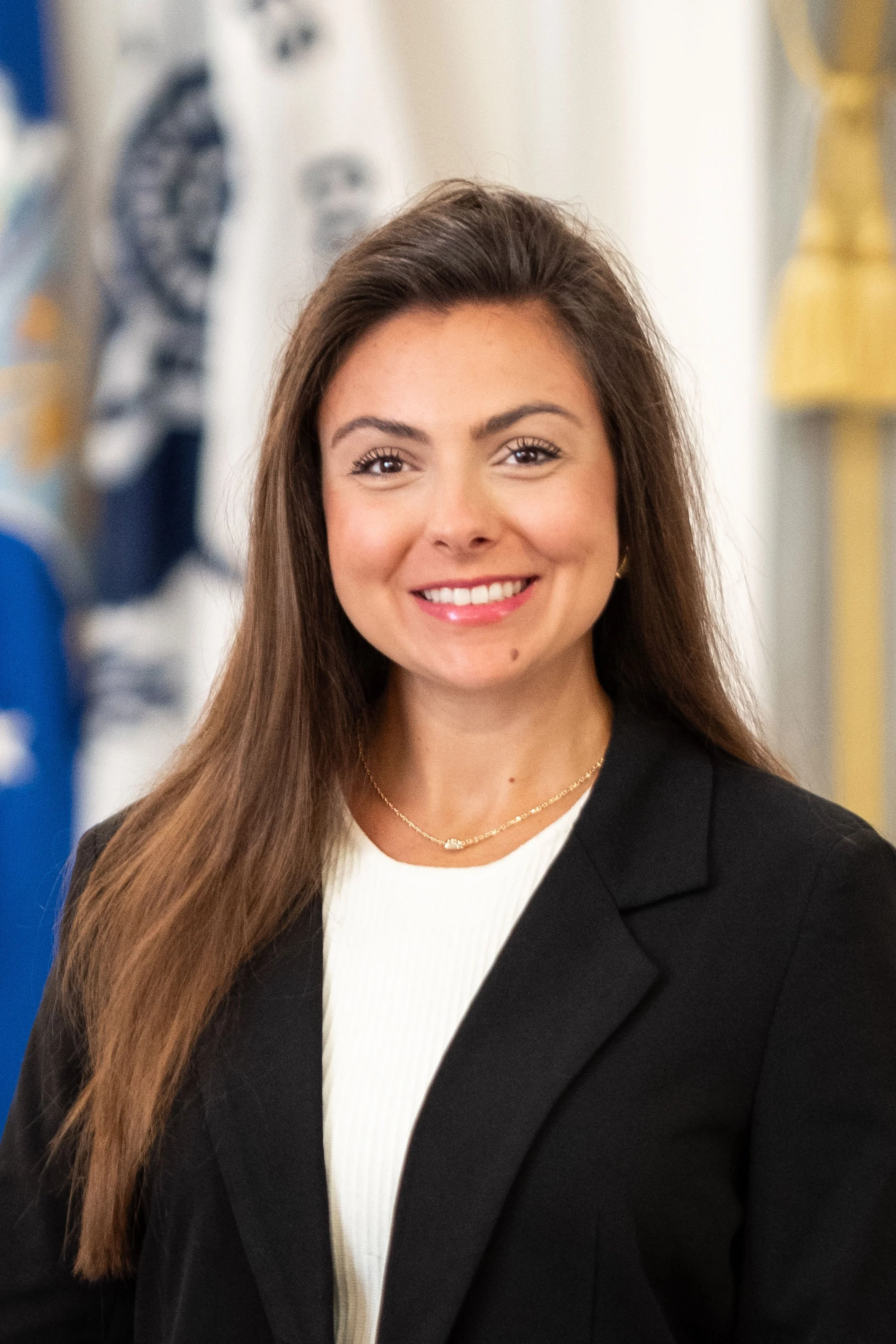 A person smiling in front of a U.S. flag