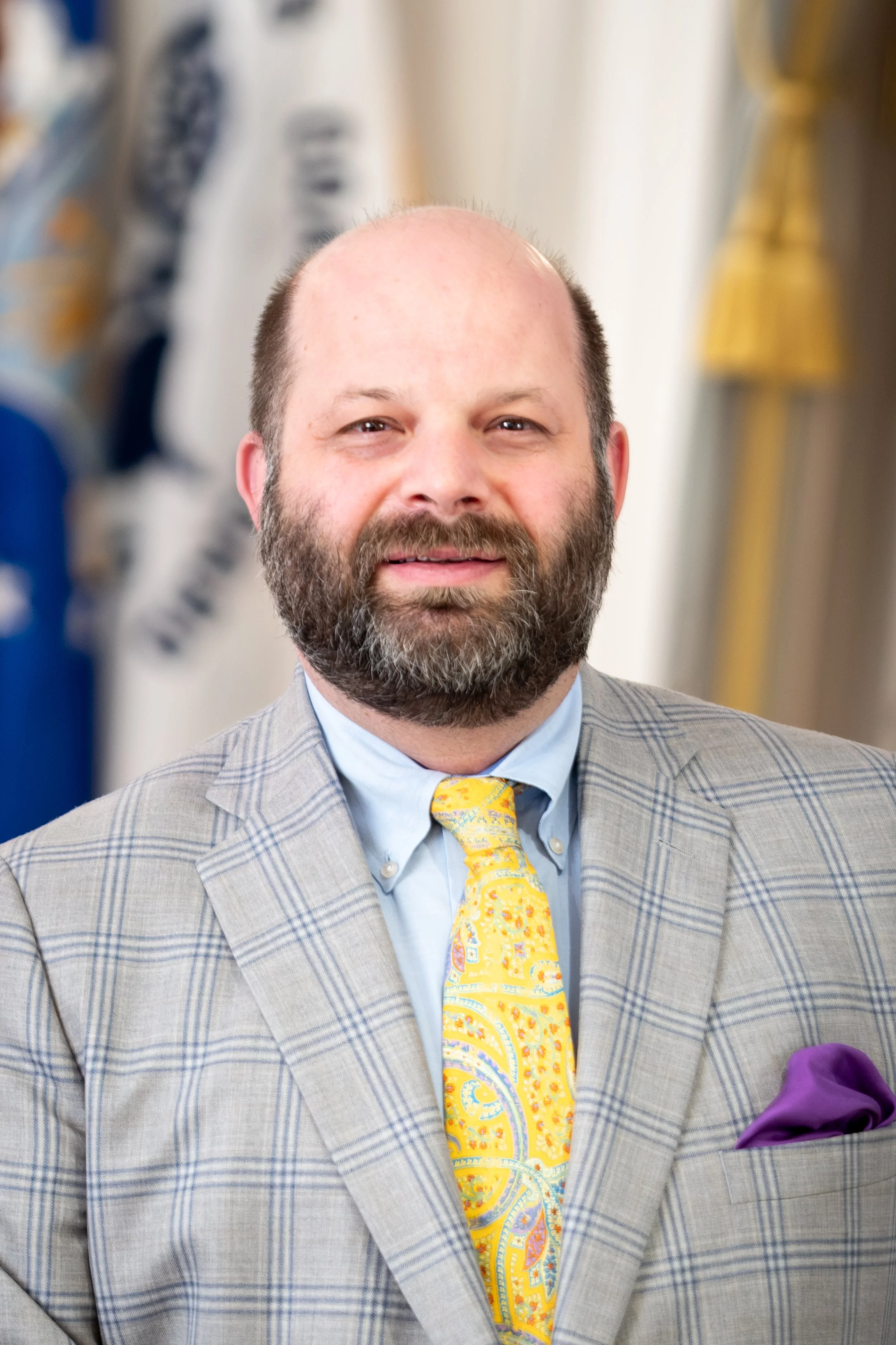 Man in a suit with striped tie and badge in front of a speckled wall