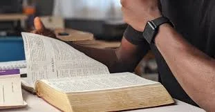 Person reading a large open Bible at a wooden table