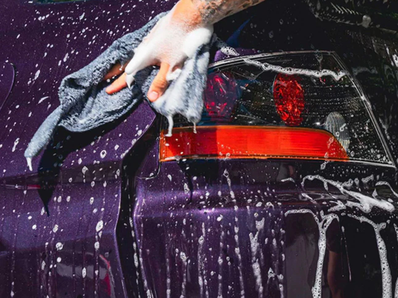 Modern wooden house with large glass window, surrounded by grassy terrain, mountains in the background, and a clear sky.