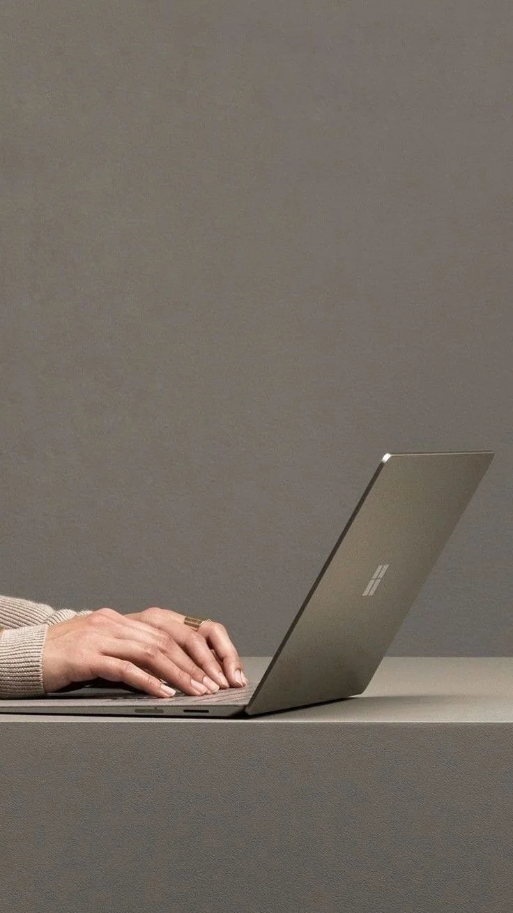 Person typing on a gray laptop on a gray surface