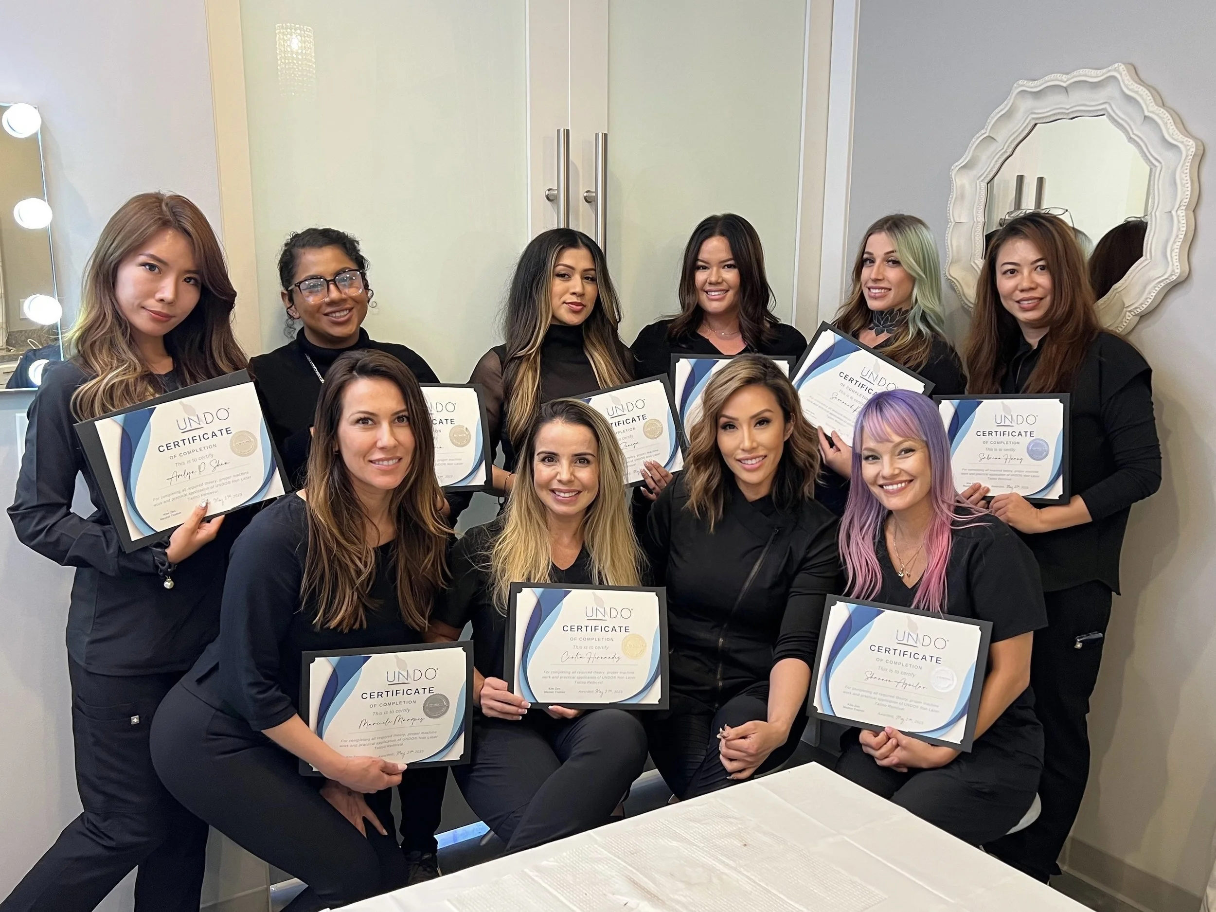 Group of individuals holding certificates in a professional setting, standing and kneeling, smiling for a photo.
