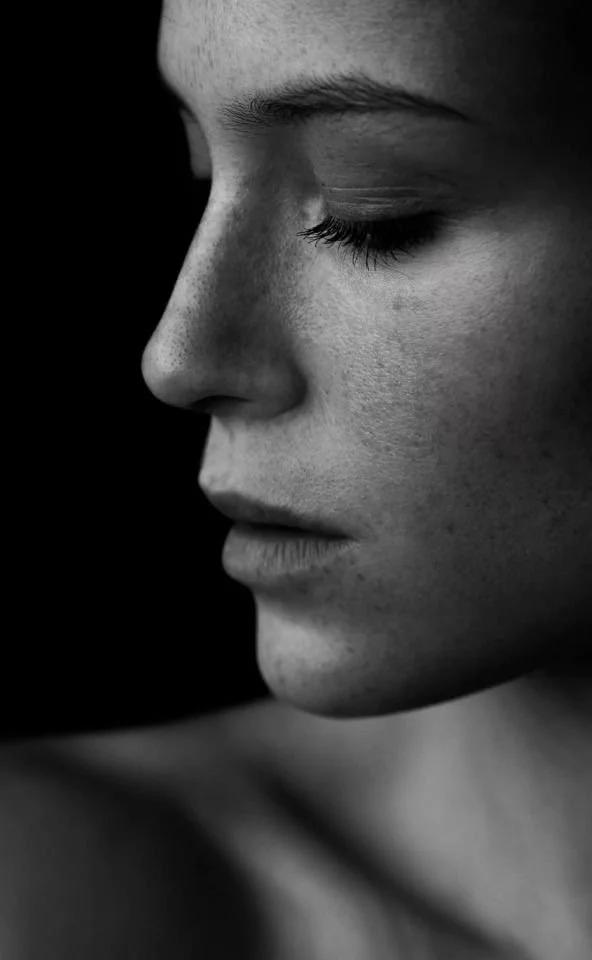 Close-up black and white portrait of a person's face with closed eyes and soft-focus lighting.