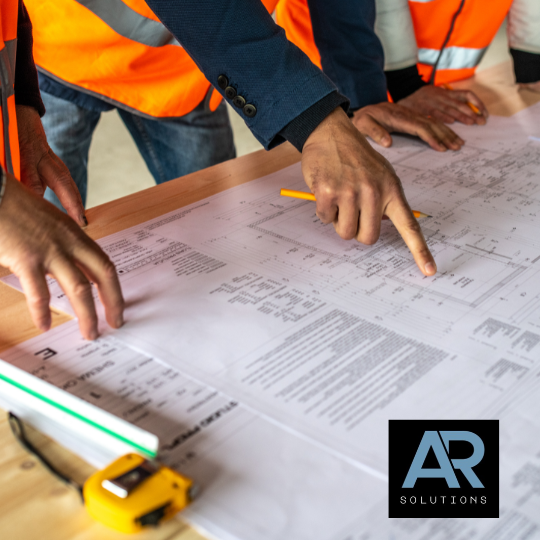 People in safety vests gathered around a table reviewing large blueprints, with a person pointing at the plans.