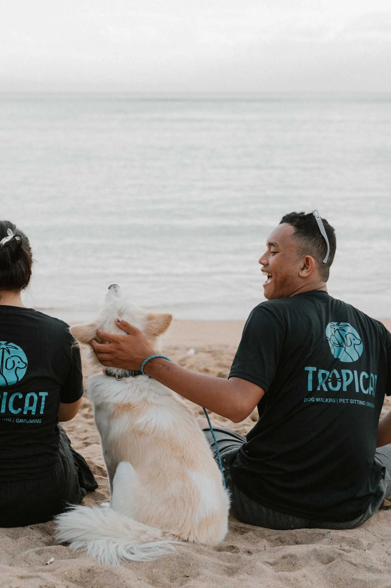 Tropicat dog walker cuddling with a dog on Sanur beach looking happy