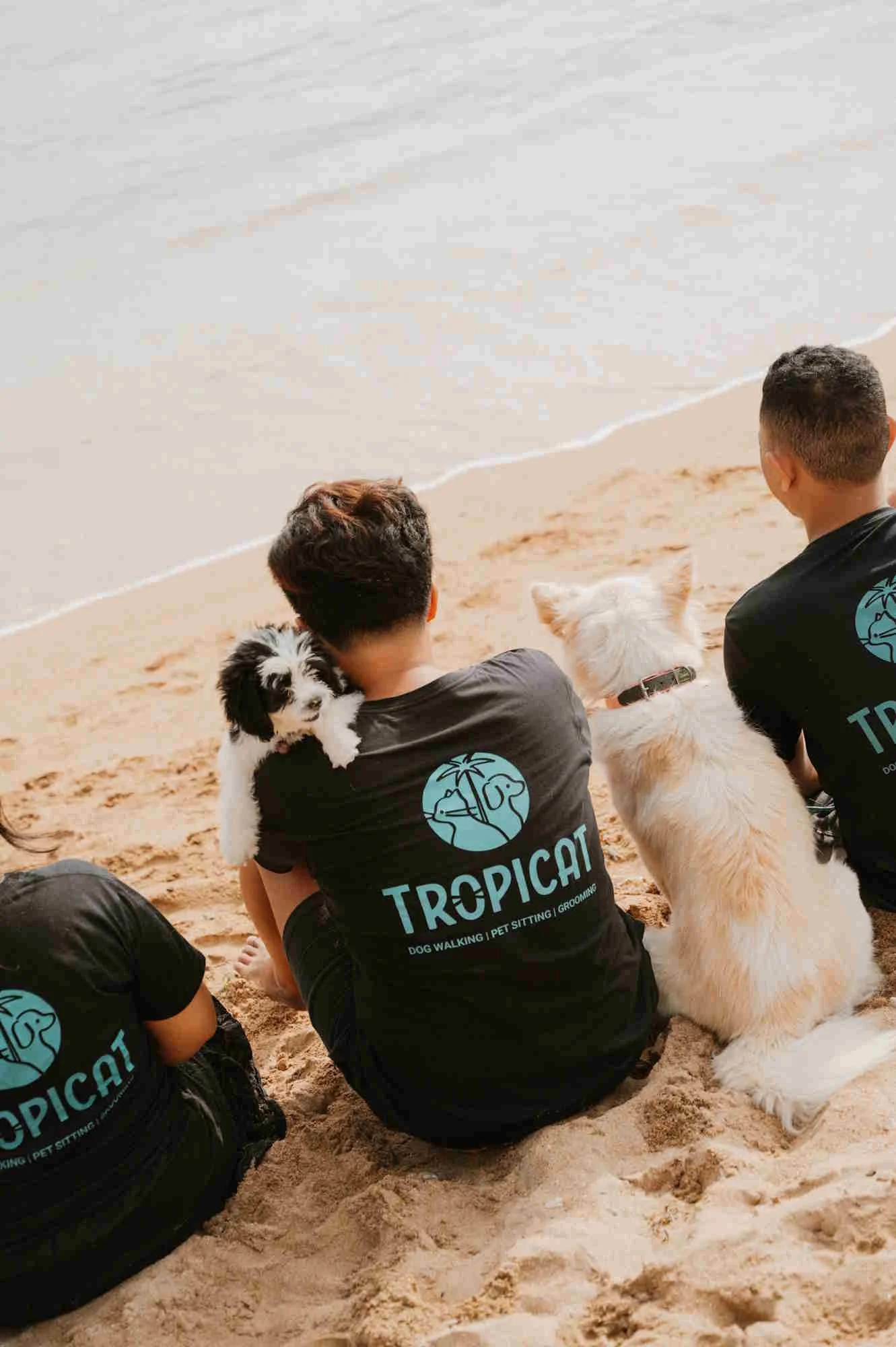 Tropicat dog walker sitting next to a dog and holding a puppy on Sanur beach