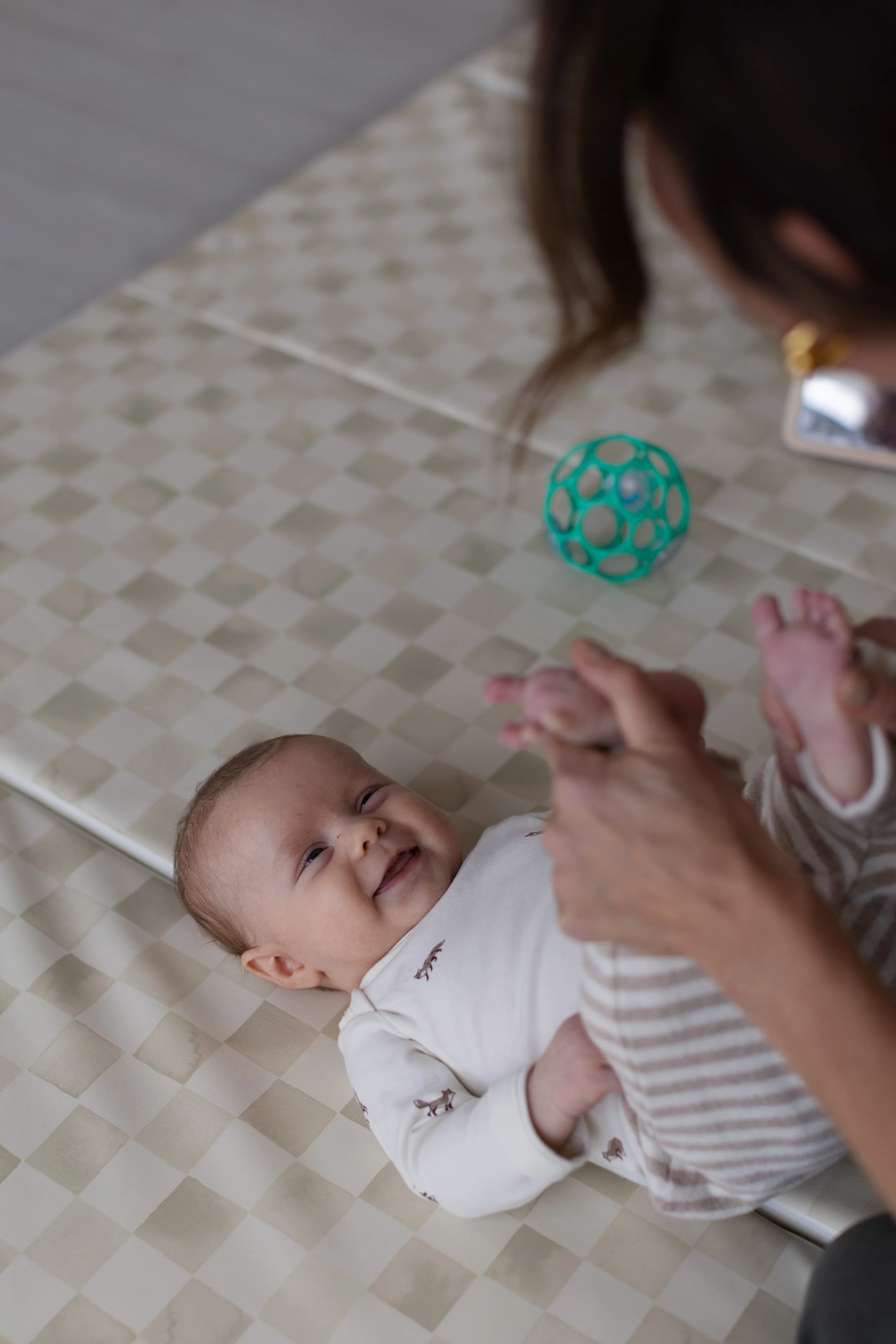 Infant engaged in hands-to-feet play during a pediatric bodywork session supporting sensory and motor development
