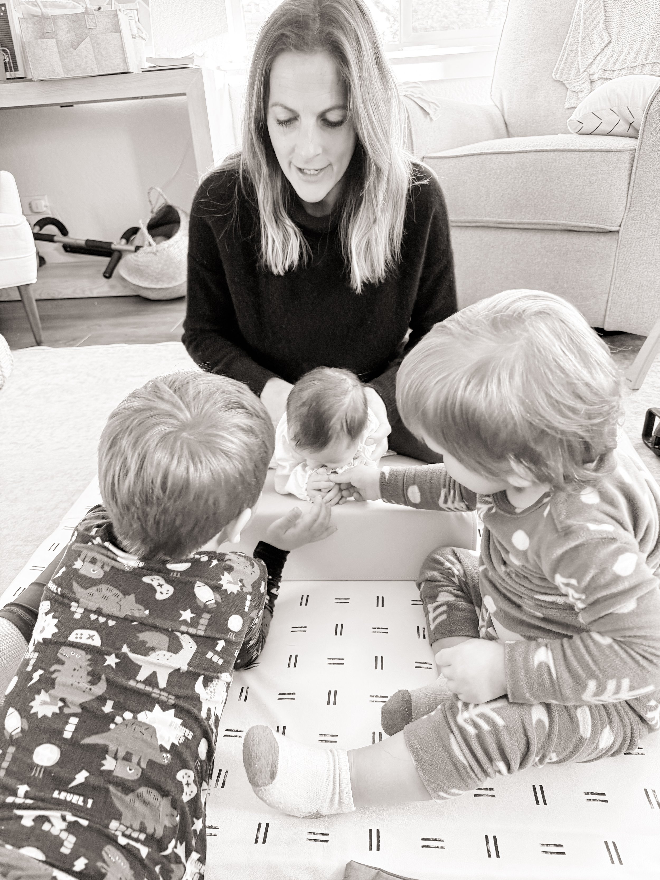 Caregiver on the floor doing active play with two siblings, demonstrating varied floor time positions for healthy infant and toddler development
