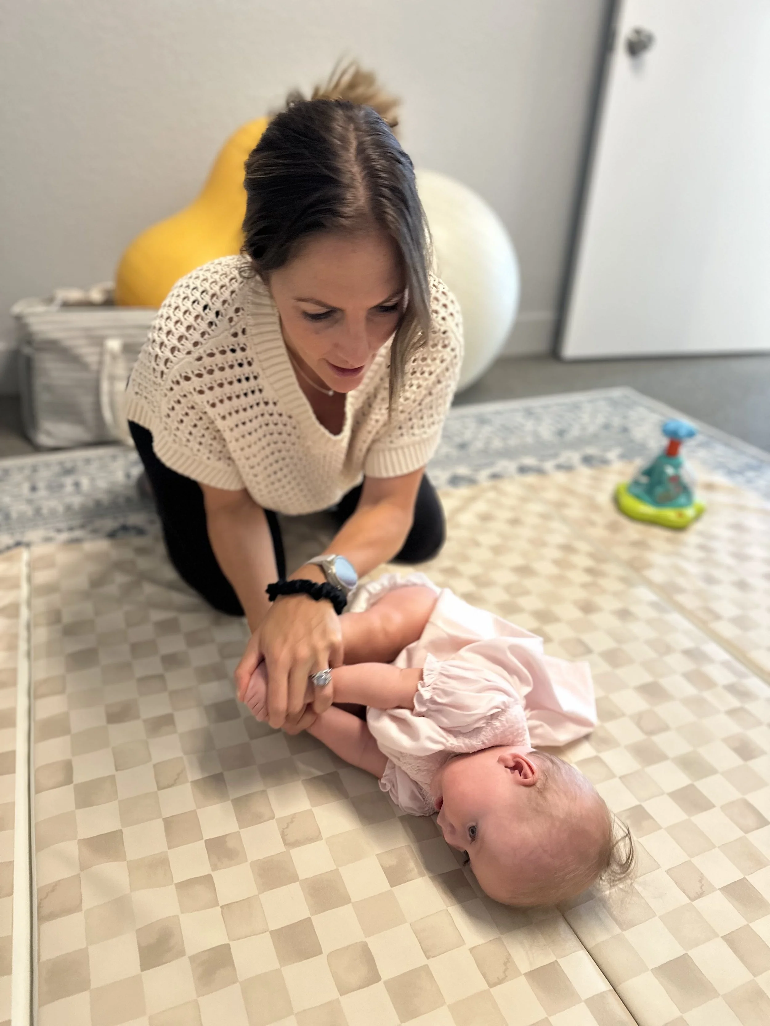 Dr. Nicole, pediatric physical therapist at Movevery in Denver, performing neuromuscular re-education with an infant in a pink outfit, gently working through the baby's legs and hips during a therapeutic activity session on a play mat
