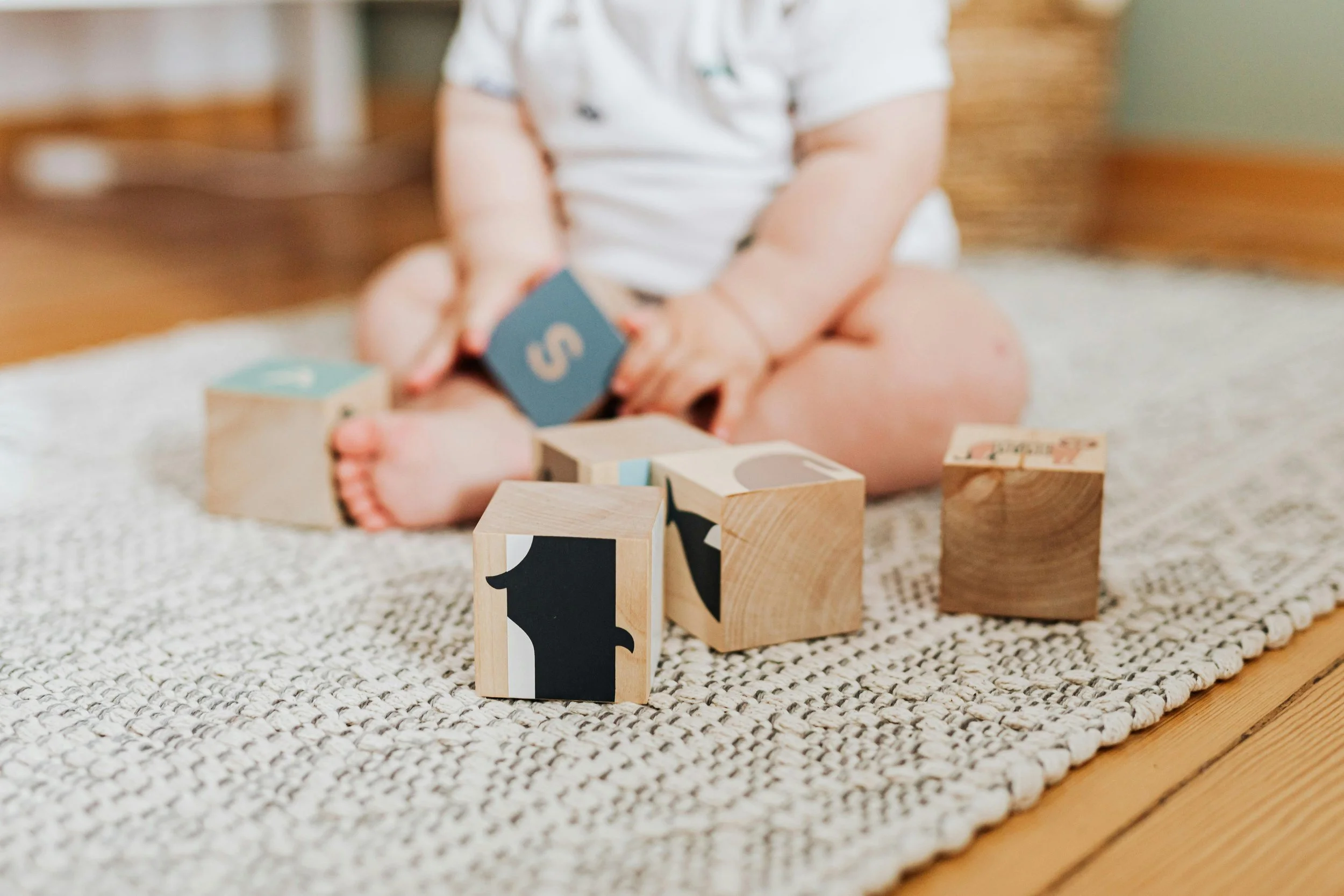 Baby sitting independently on the floor playing with wooden blocks — floor time in a variety of positions supports sensory development, strength, and healthy head shape