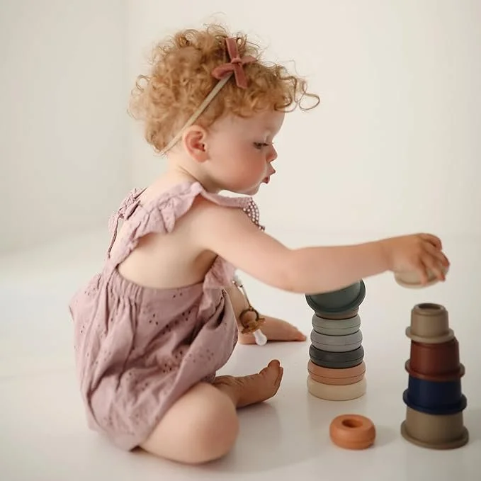 Baby happily playing with Mushie Stacking Cups Toy, made in Denmark. Original minimalist design that supports sensory development, motor skills, and safe play.