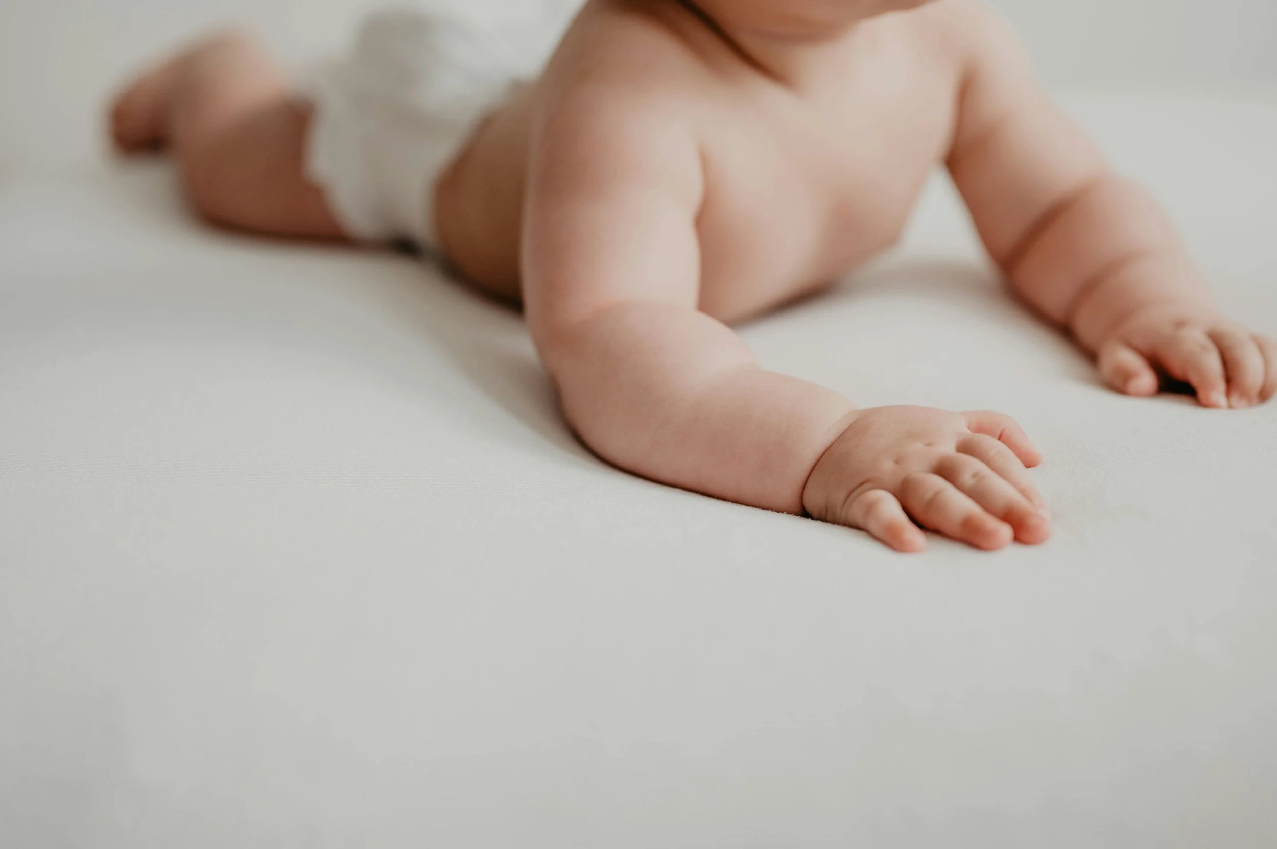 Baby during supervised tummy time, weight bearing through arms and hands on a white surface — a key position for preventing flat head and building early strength