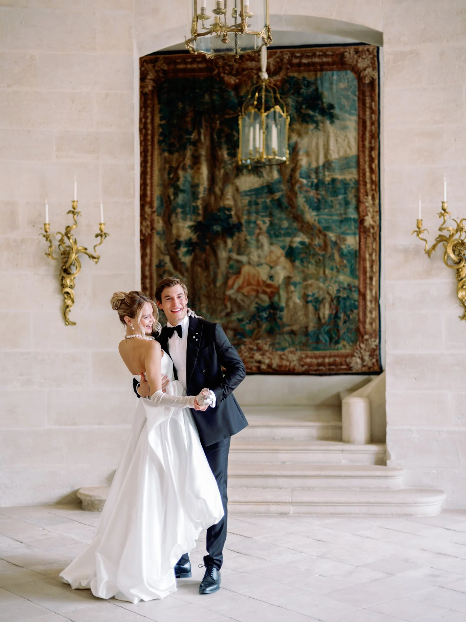 Bride and groom dancing during a wedding at Château de Villette in France, framed by the château's iconic historic tapestry, ornate wall sconces, and elegant stone interior.