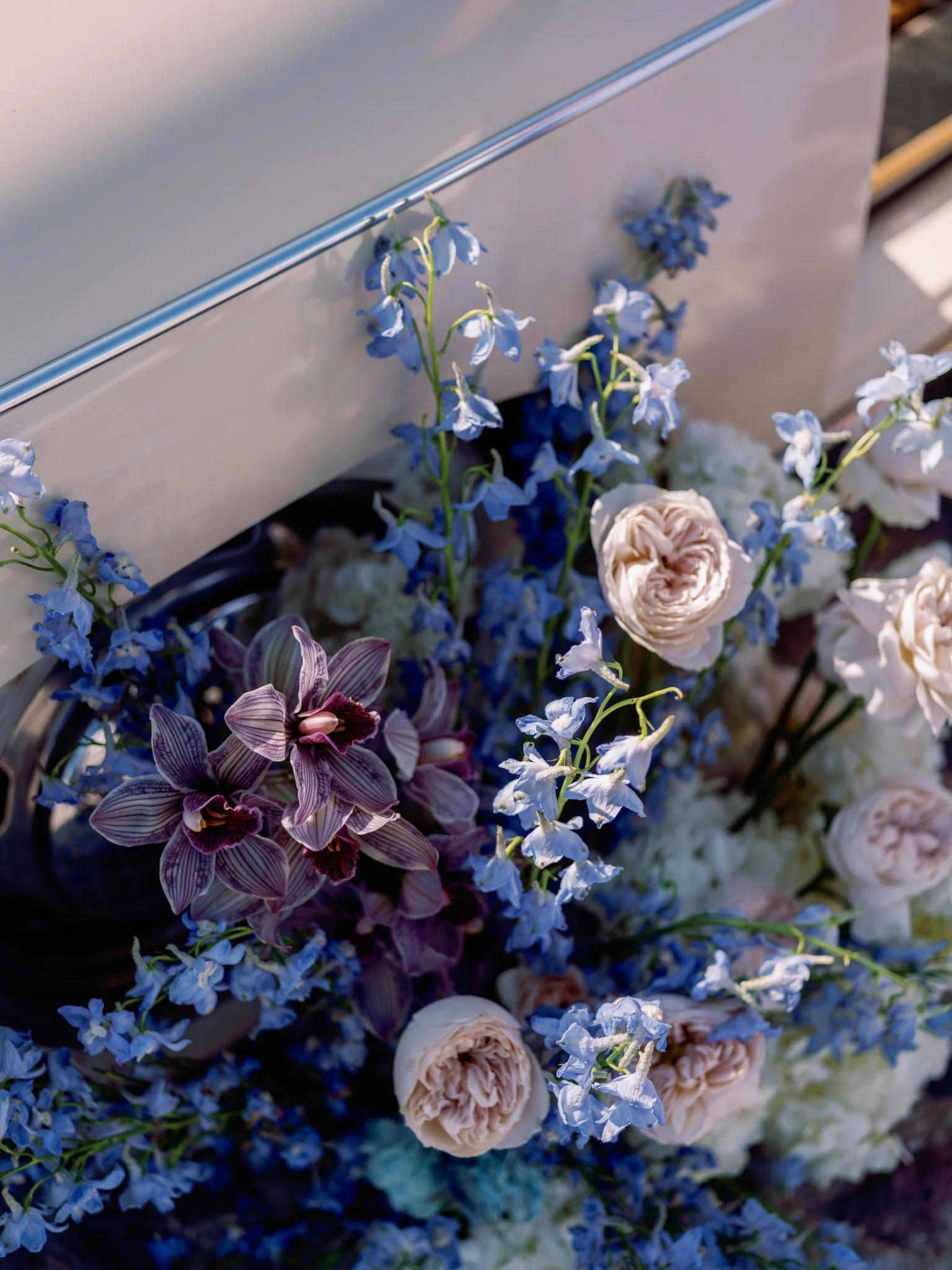 Vintage Porsche adorned with a romantic arrangement of roses, orchids, delphiniums, and hydrangeas in rich shades of blue, lavender, and soft blush during a couples engagement session in Greece.