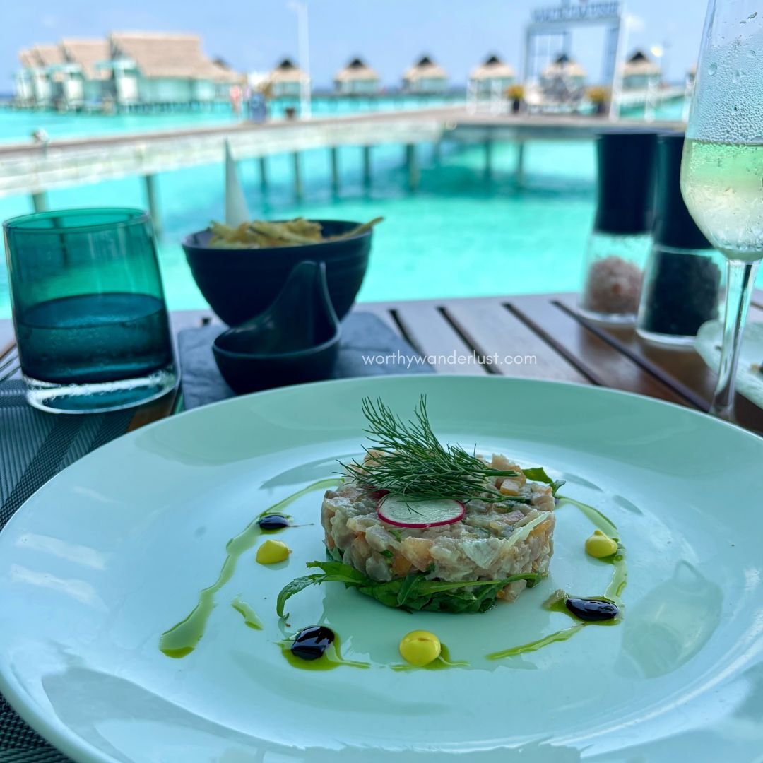 Tuna tartare dish with turquoise water and overwater villas in the background