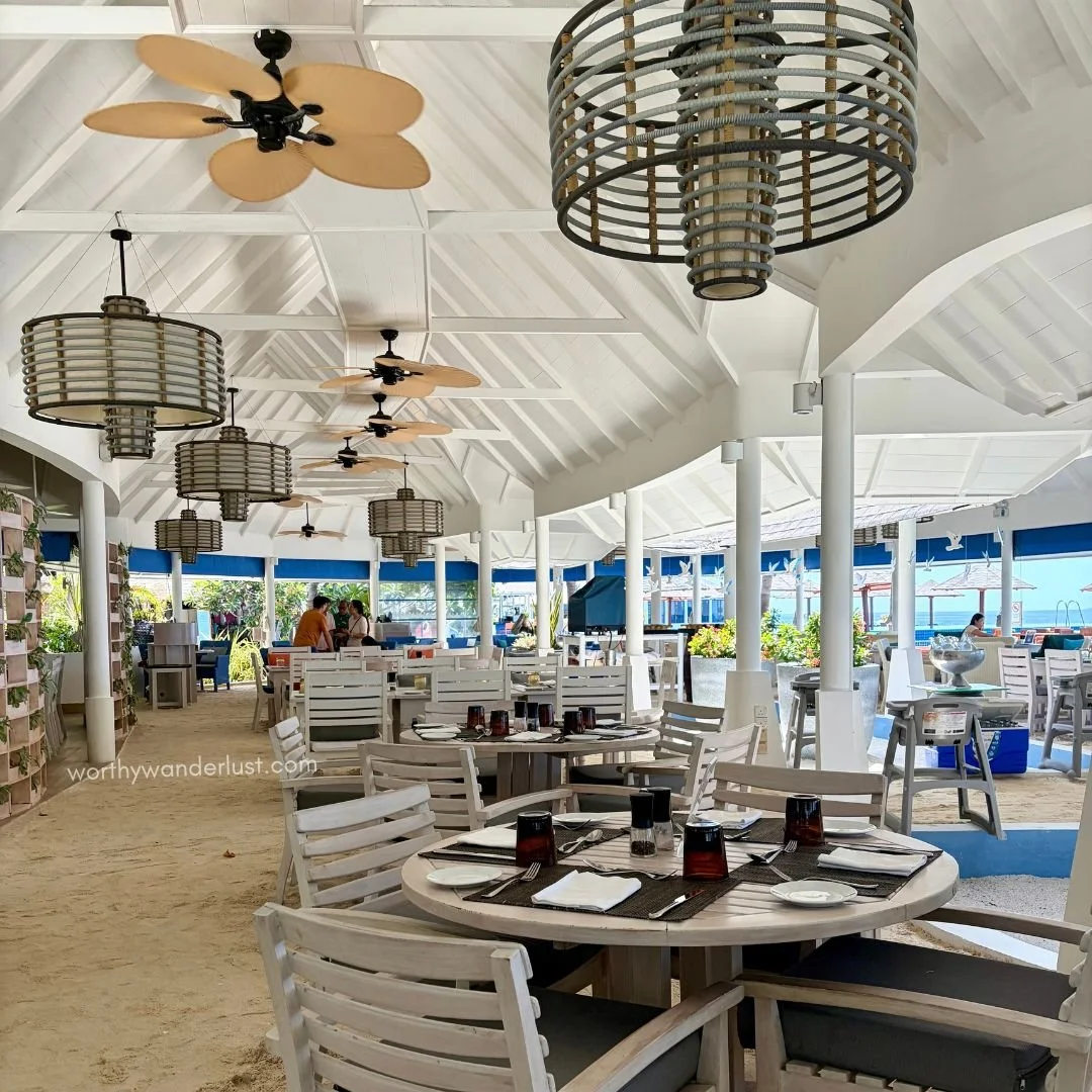 Restaurant with white high ceiling, white chairs and sandy beach flooring