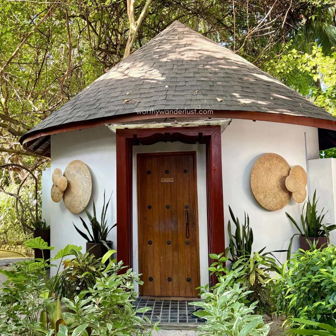 Picture of a hut surrounded by greenery and large wall art.