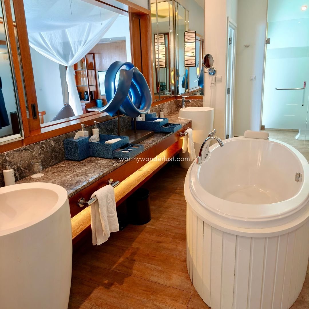 A bathroom with a bathtub, two sinks and view towards bedroom.
